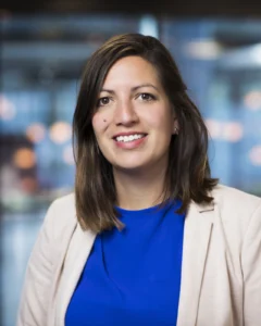 Dr Hendriks, medium length brown hair, brown eyes, smiling, blue shirt and light blazer